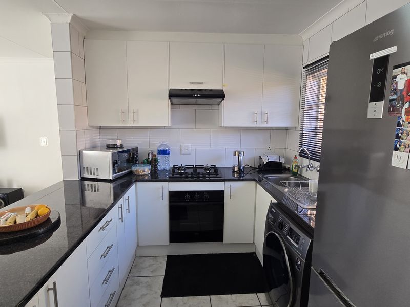 Compact kitchen featuring white cabinetry, dark granite countertops, a gas hob, built-in oven, and integrated laundry plumbing, opening into the adjacent living area.