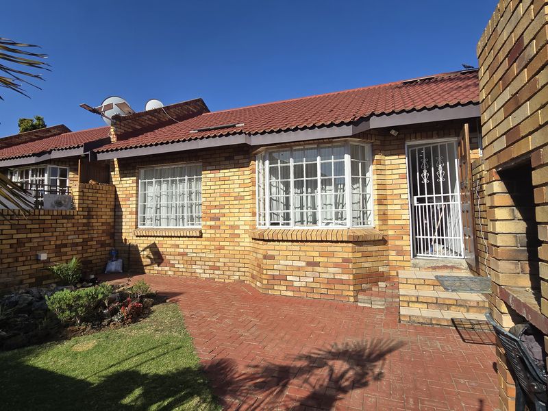 Rear exterior view of the townhouse featuring a brick facade, paved patio area, built-in brick braai, and a small garden.