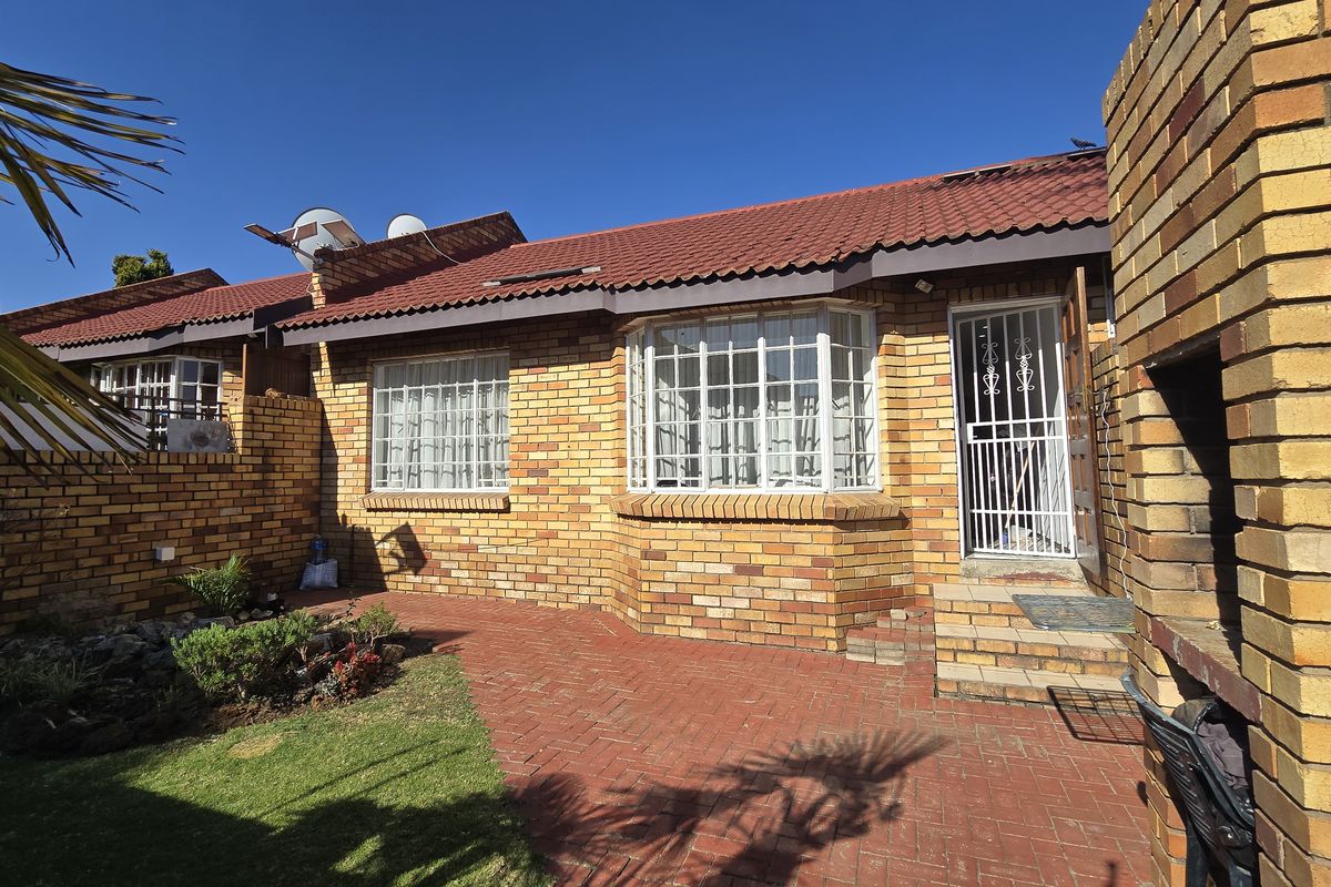 Rear exterior view of the townhouse featuring a brick facade, paved patio area, built-in brick braai, and a small garden.