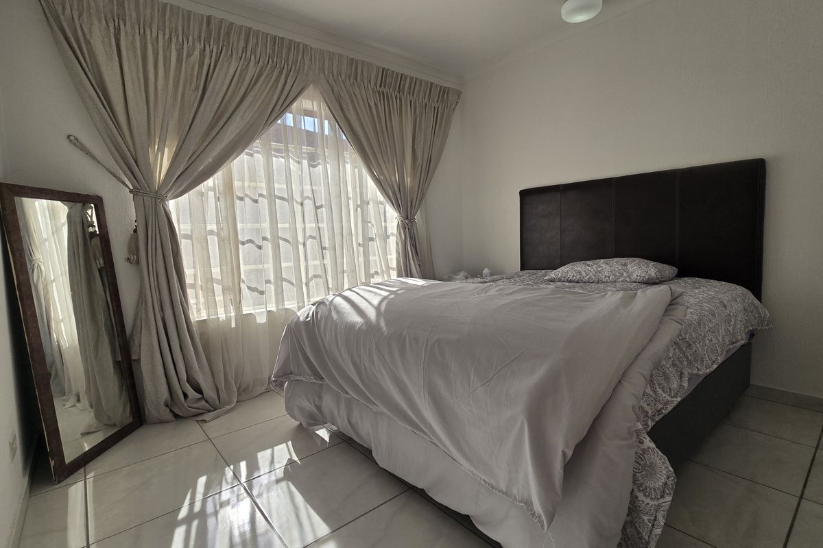 A functional bedroom featuring tiled flooring and natural light through large windows with installed curtain rails.