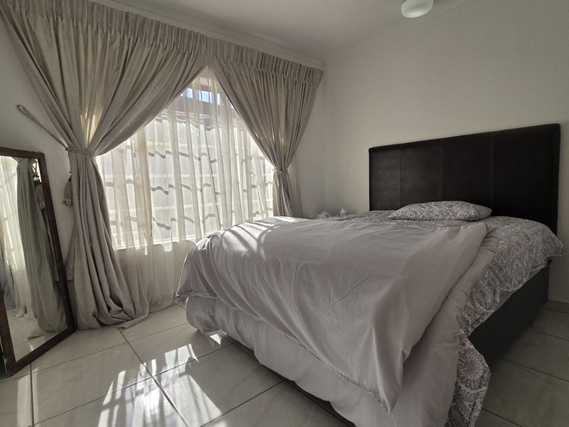 A functional bedroom featuring tiled flooring and natural light through large windows with installed curtain rails.