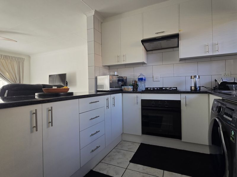 Open-plan kitchen featuring white cabinetry, granite countertops, built-in oven, and gas hob, seamlessly flowing into the adjacent living area.