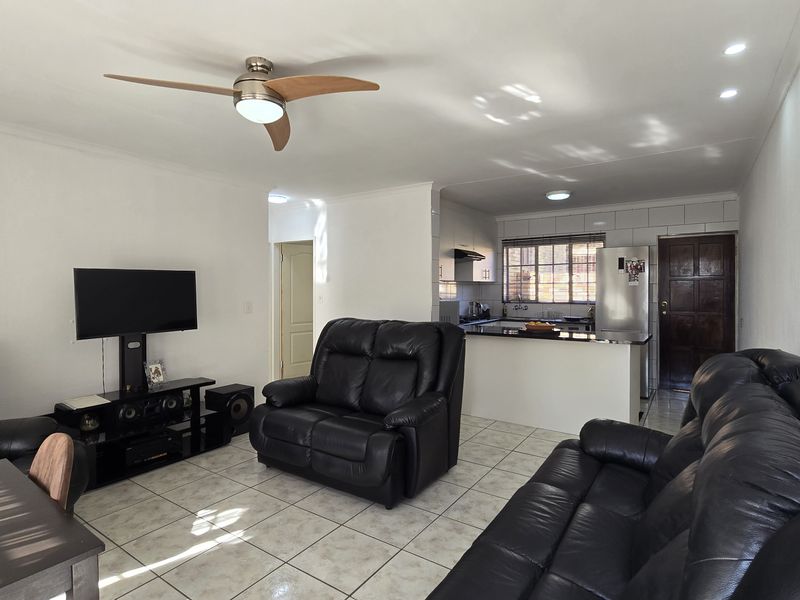 Open-plan living area featuring tiled floors, a ceiling fan, and a functional kitchen with built-in cabinetry and countertops.