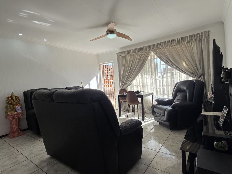 A bright living room featuring tiled flooring, a ceiling fan, and recessed lighting, with direct access to an outdoor area through a security gate.
