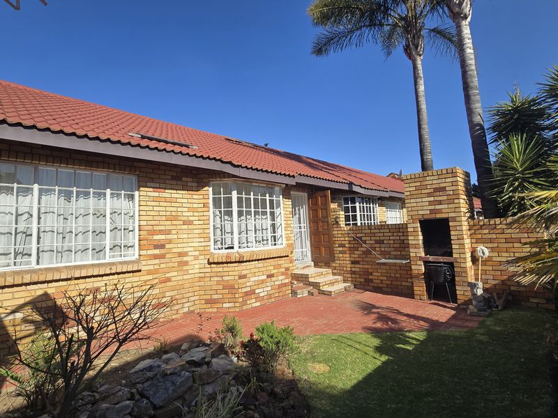 Rear exterior view of the townhouse featuring a brick facade, tiled roof, paved patio area, and a built-in brick braai.