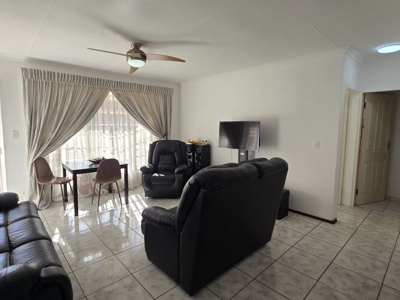 A bright living room featuring tiled flooring, a ceiling fan, and a large sliding glass door providing access to the exterior.