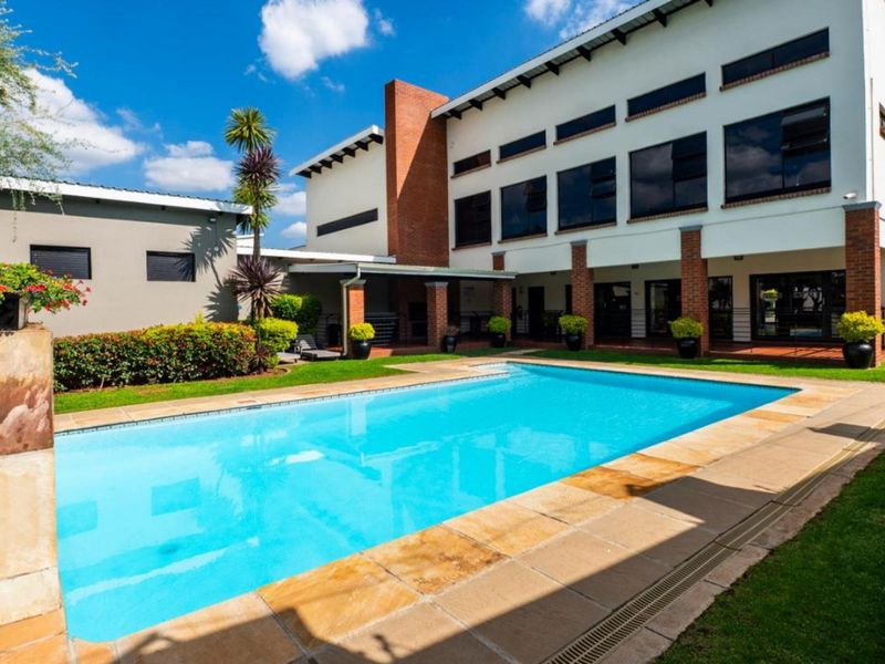 A well-maintained swimming pool area featuring stone coping, brick architectural details, and a covered patio overlooking a landscaped garden.
