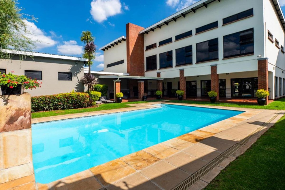 A well-maintained swimming pool area featuring stone coping, brick architectural details, and a covered patio overlooking a landscaped garden.