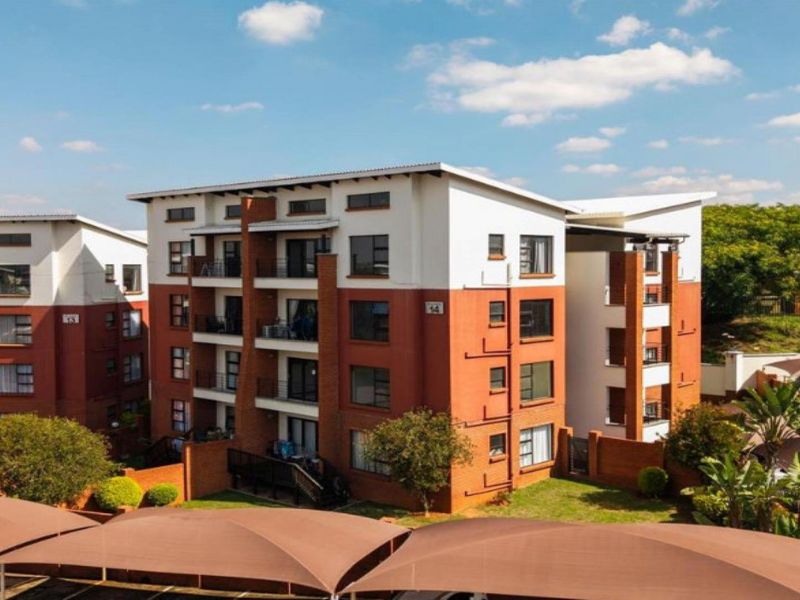 Exterior view of a multi-story apartment complex featuring brick and white facade finishes, private balconies, and covered parking bays.