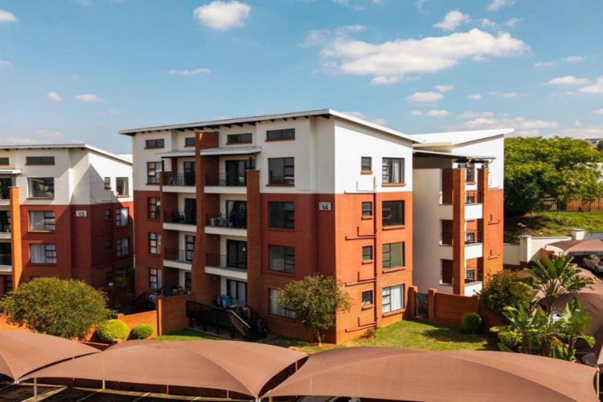Exterior view of a multi-story apartment complex featuring brick and white facade finishes, private balconies, and covered parking bays.