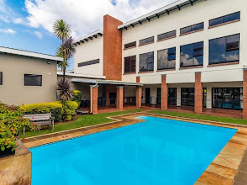 A well-maintained outdoor pool area featuring a swimming pool, stone paving, and a covered patio area with a brick chimney structure.