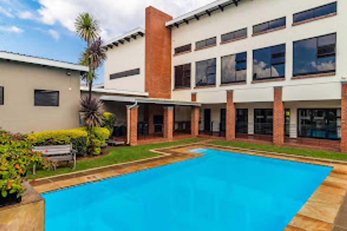 A well-maintained outdoor pool area featuring a swimming pool, stone paving, and a covered patio area with a brick chimney structure.
