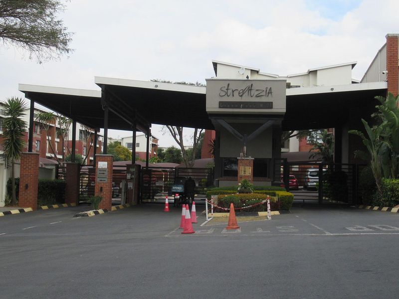 Main entrance and security gatehouse for the Strelitzia apartment complex, featuring controlled access, brick masonry, and paved driveway.