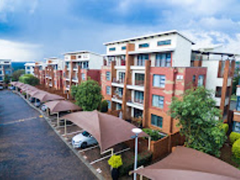 An elevated view of a modern multi-story apartment complex featuring brick facades, balconies, and a paved parking area with covered bays.