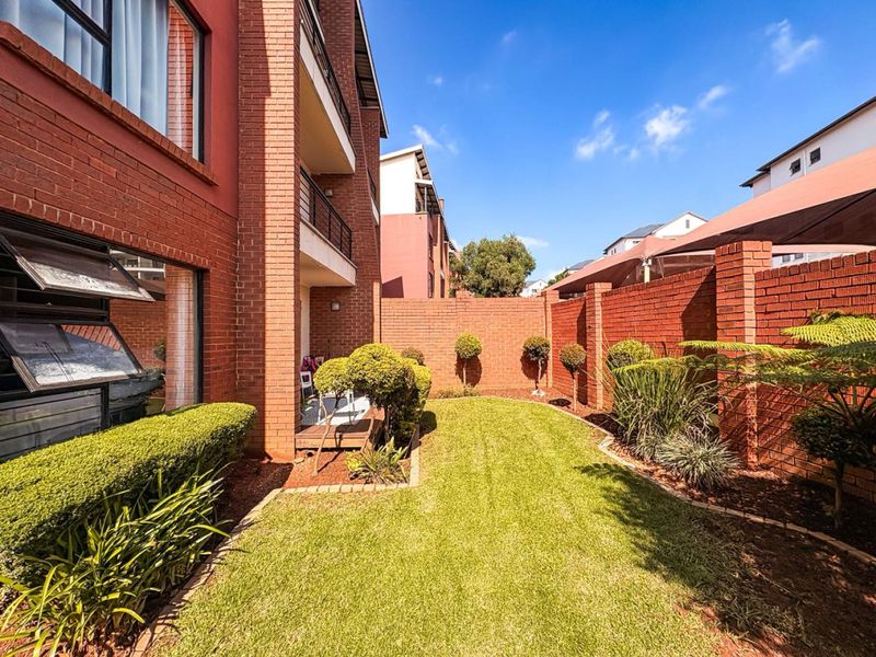 A well-maintained rear garden area featuring a manicured lawn, brick boundary walls, and a covered patio section attached to the apartment building.