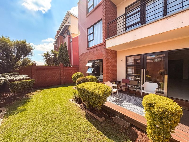 A well-maintained rear exterior view featuring a private garden, a tiled patio area, and direct access to the apartment through sliding glass doors.