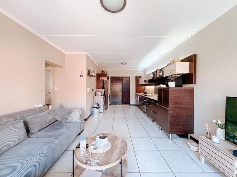 Open-plan living area featuring a modern kitchen with built-in cabinetry, integrated appliances, and tiled flooring throughout the combined space.