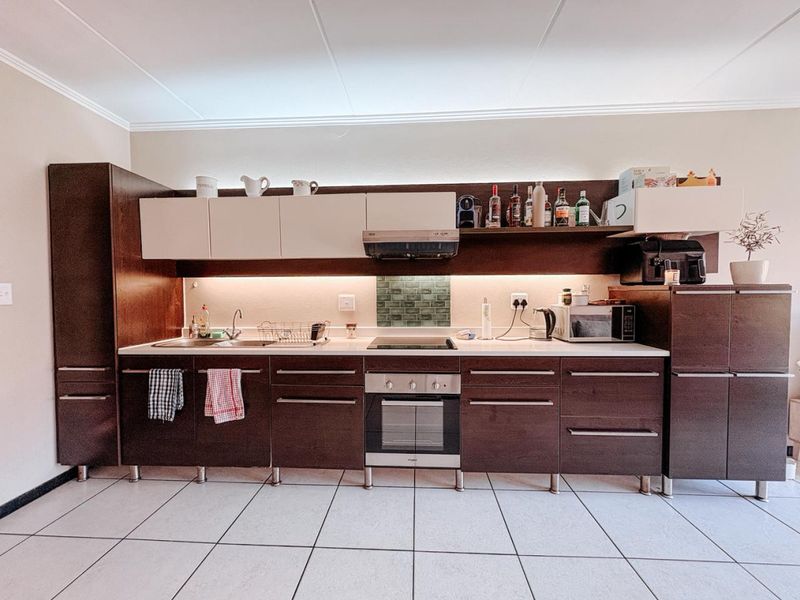 A modern kitchen featuring dark wood cabinetry, white upper cabinets, integrated appliances including an oven and hob, and tiled flooring with under-cabinet lighting.
