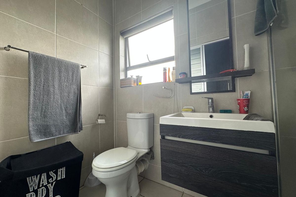 A functional bathroom featuring a wall-mounted vanity with basin, toilet, and neutral wall tiling, providing a clean and modern aesthetic.