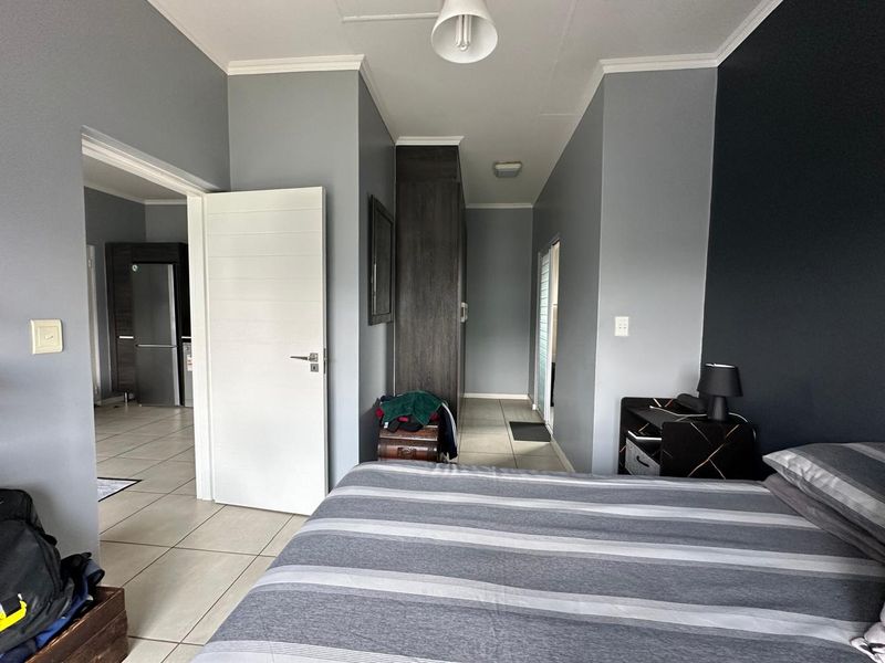 A well-maintained bedroom featuring neutral grey walls, built-in storage cupboards, and tiled flooring, with direct access to an adjacent living area.