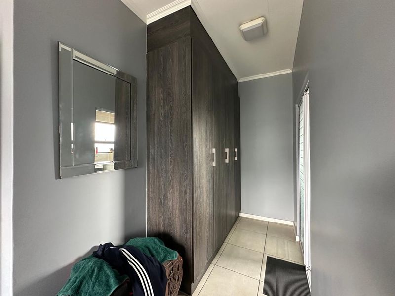 A well-maintained hallway featuring dark wood-grain built-in cabinetry, neutral tiled flooring, and a sliding door providing access to the exterior.