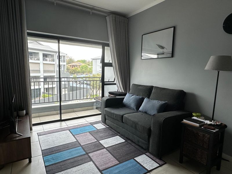 A well-maintained living room featuring tiled floors and a large sliding glass door that opens onto a private balcony.