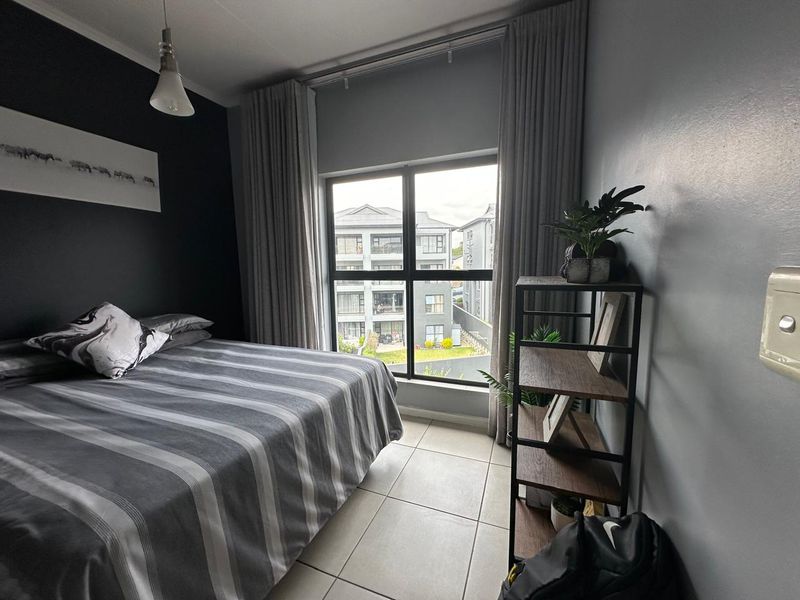 A well-maintained bedroom featuring neutral tiled flooring, a large window with floor-to-ceiling curtains, and a modern pendant light fixture.