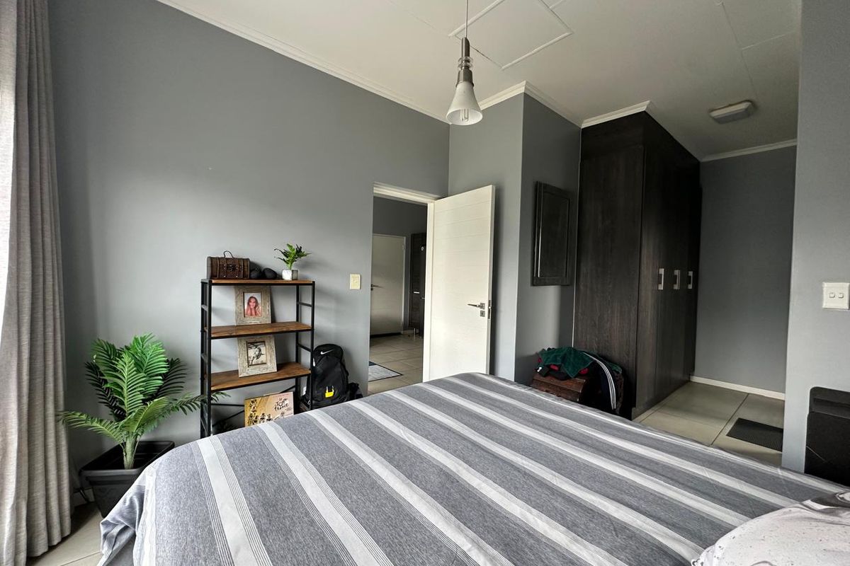 A well-maintained bedroom featuring dark wood built-in cupboards, neutral grey walls, tiled flooring, and a modern pendant light fixture.
