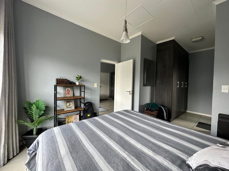A well-maintained bedroom featuring dark wood built-in cupboards, neutral grey walls, tiled flooring, and a modern pendant light fixture.