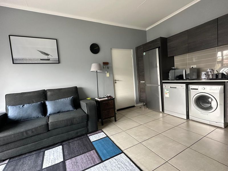Open-plan living area featuring a modern kitchen with dark cabinetry, tiled flooring, and integrated appliances, seamlessly connected to a comfortable lounge space.