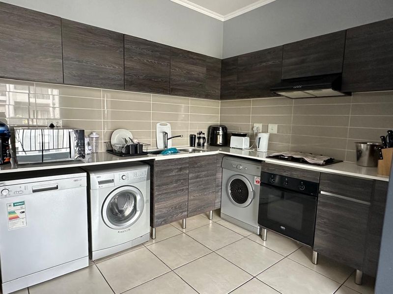 Modern kitchen featuring dark wood-grain cabinetry, tiled backsplash, integrated oven and hob, and dedicated space for laundry appliances.
