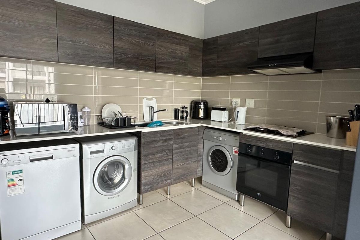 Modern kitchen featuring dark wood-grain cabinetry, tiled backsplash, integrated oven and hob, and dedicated space for laundry appliances.