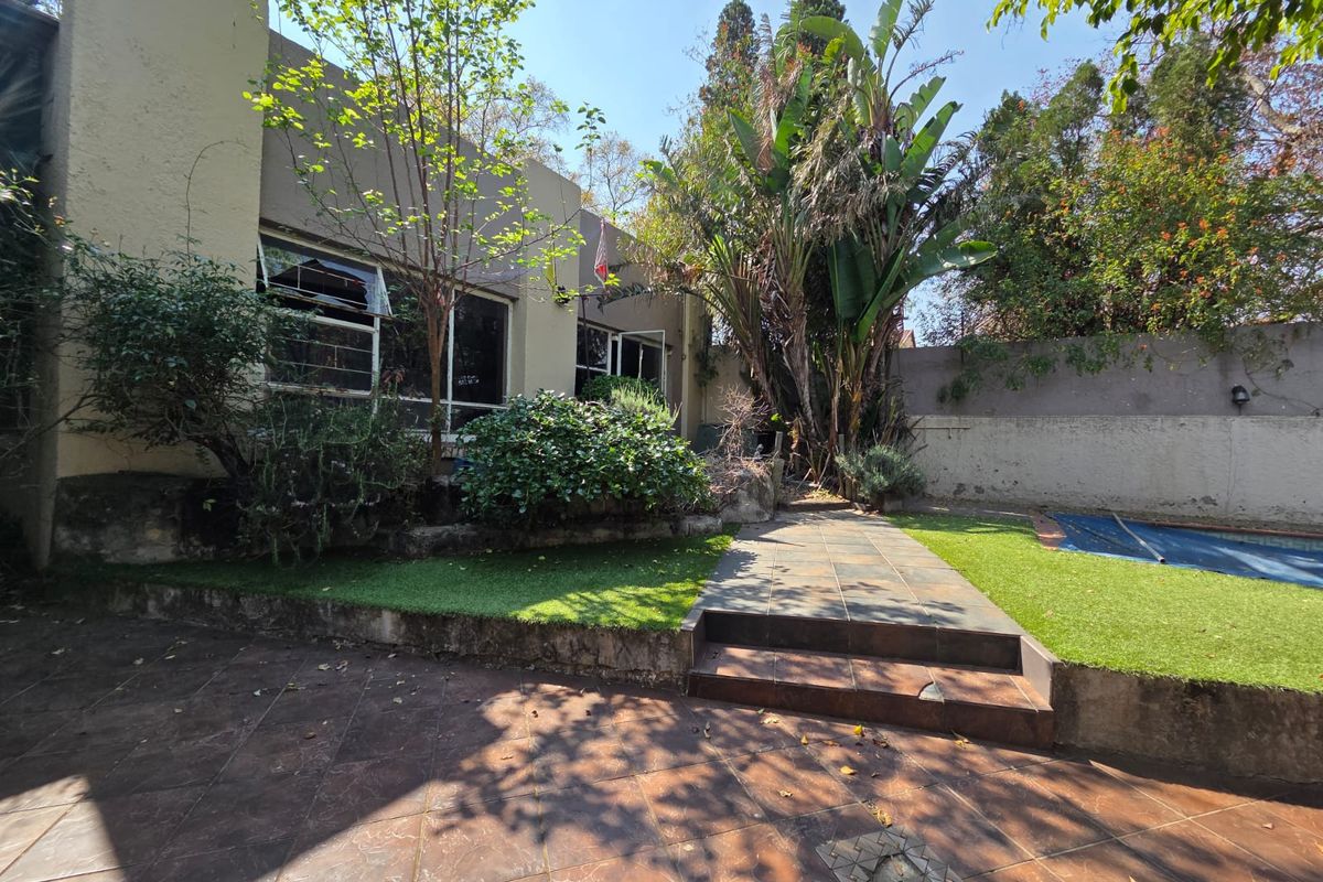 Rear garden area featuring a tiled patio, swimming pool with cover, and tiered landscaping with retaining walls.