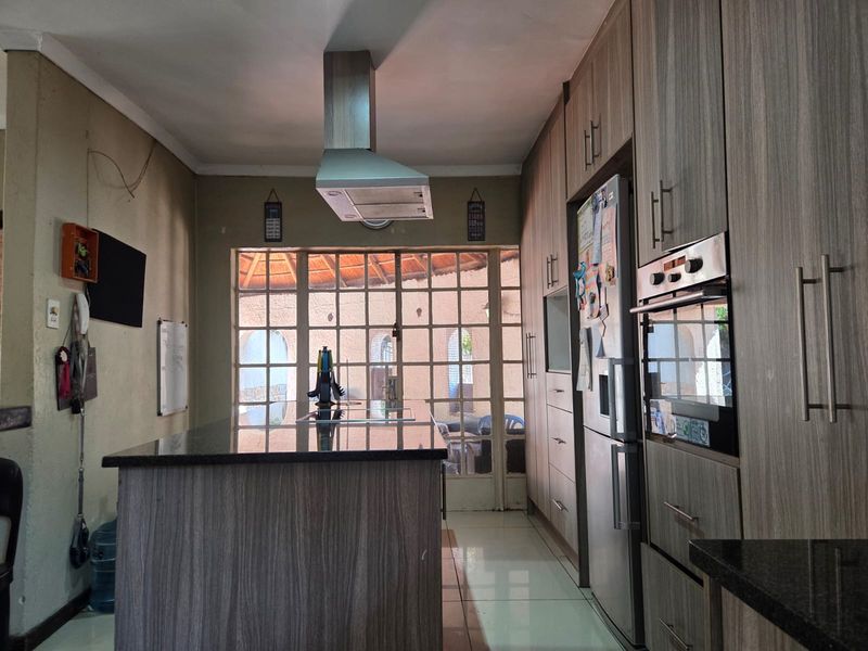 A functional kitchen featuring wood-look cabinetry, a central island with granite countertops, built-in oven, and an extractor fan, leading to an outdoor patio area.