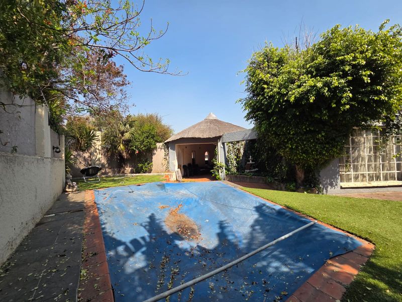 Outdoor pool area featuring a swimming pool with a cover and an adjacent thatched lapa structure set within a private garden.