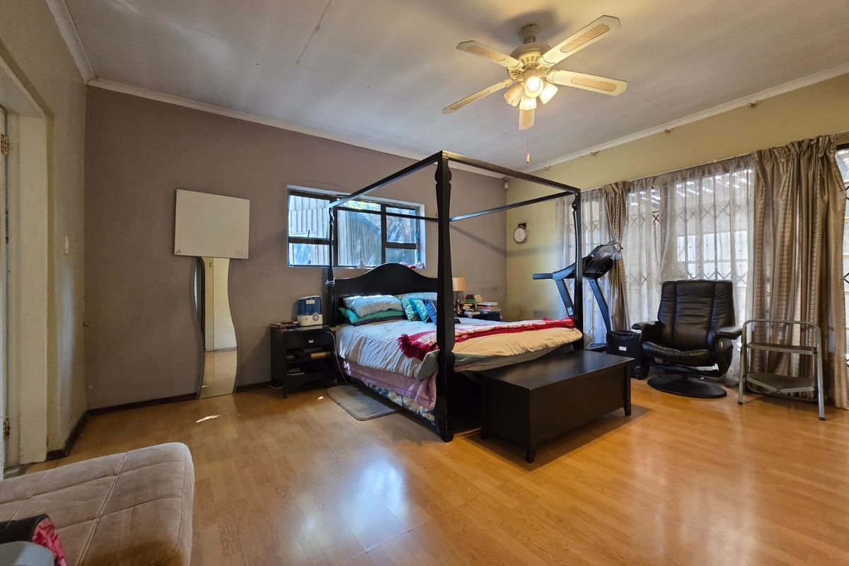 Spacious bedroom featuring laminate flooring, a ceiling fan, and large windows with security gates, offering a functional layout with potential for cosmetic updates.