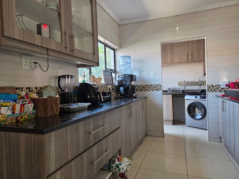 A functional kitchen featuring granite countertops, modern laminated cabinetry, and a tiled backsplash, with an adjoining scullery area containing laundry facilities.