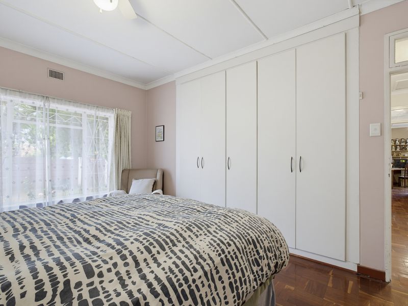 A bedroom featuring parquet flooring, built-in cupboards, and a ceiling fan, with a view into the adjacent hallway.