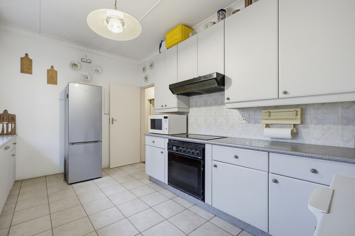 A functional kitchen featuring white cabinetry, laminate countertops, tiled flooring, and built-in cooking appliances including an oven, hob, and extractor fan.