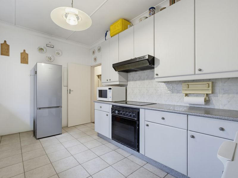 A functional kitchen featuring white cabinetry, laminate countertops, tiled flooring, and built-in cooking appliances including an oven, hob, and extractor fan.