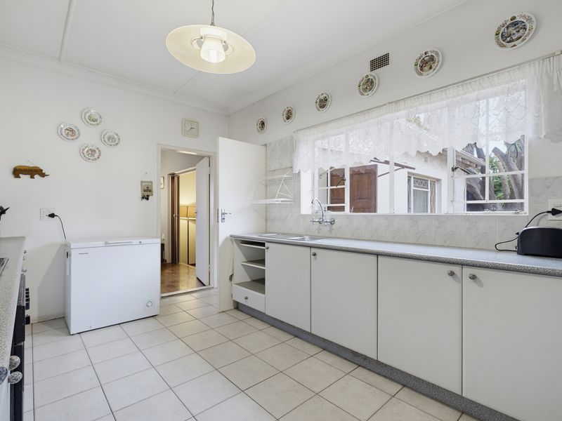 A functional kitchen featuring laminate countertops, built-in cabinetry, a stainless steel sink, and tiled flooring, offering a clean and practical workspace.