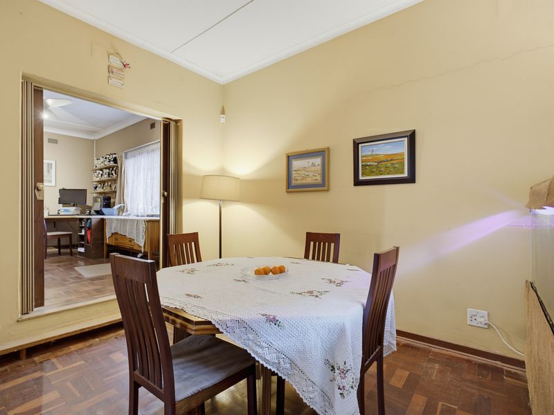 A dining room featuring parquet flooring and a sliding door leading to an adjacent room, showing signs of wall plaster cracking.