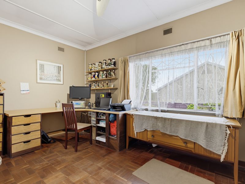 A functional home office featuring classic parquet flooring, a large window providing natural light, and integrated ventilation grilles.