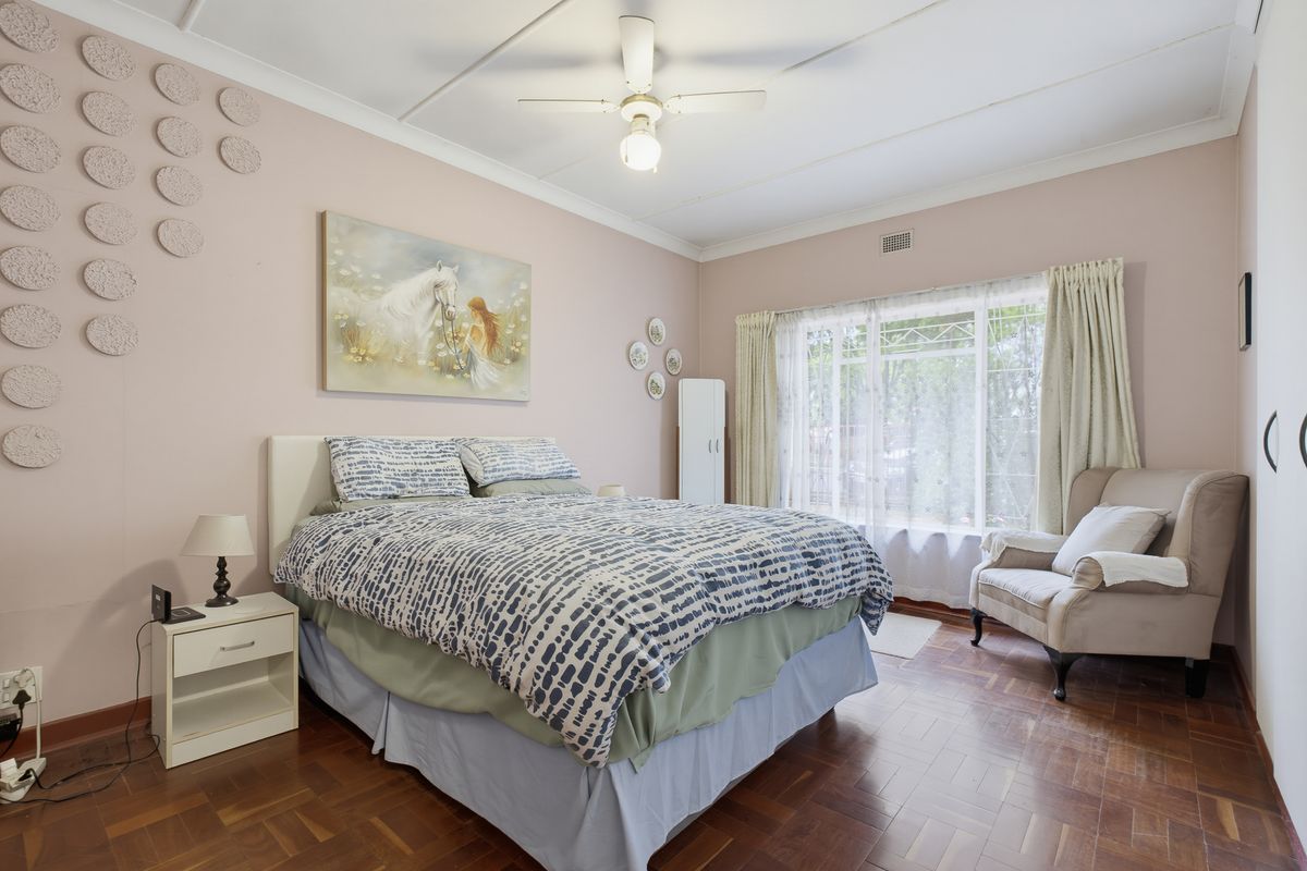 A well-lit bedroom featuring classic parquet flooring, a ceiling fan, and built-in wardrobe storage, offering a comfortable and functional living space.