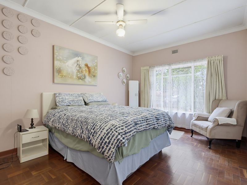 A well-lit bedroom featuring classic parquet flooring, a ceiling fan, and built-in wardrobe storage, offering a comfortable and functional living space.