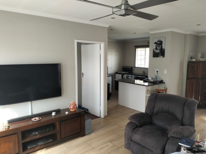 Open plan living area featuring tiled flooring, a ceiling fan, and a functional kitchen with a breakfast bar and built-in cabinetry.