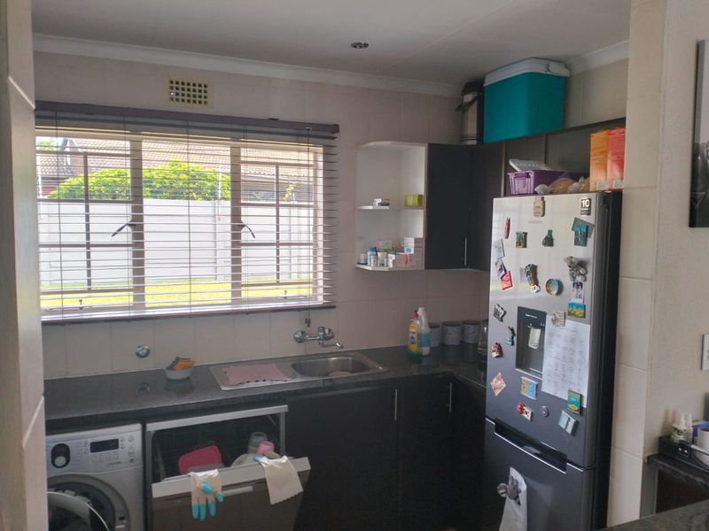 Functional kitchen area featuring dark cabinetry, granite countertops, a stainless steel sink, and tiled splashbacks with natural light from the window.