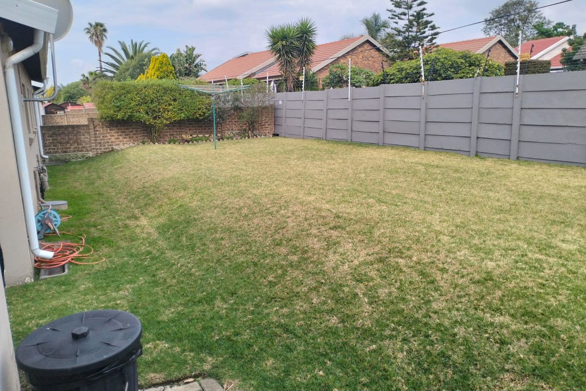A private rear garden featuring a well-maintained lawn, enclosed by a secure precast concrete boundary wall with electric fencing.