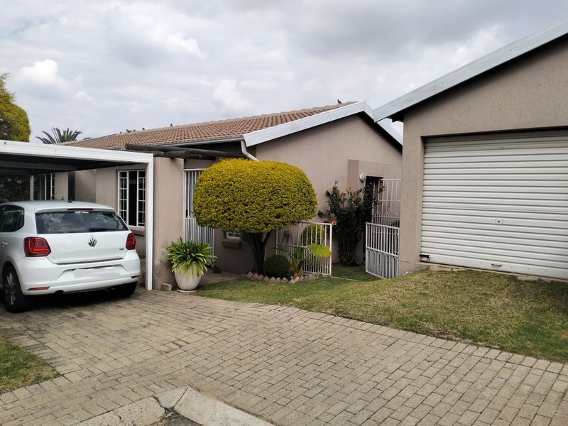 Front exterior view of the house featuring a paved driveway, carport, single garage with a roller shutter door, and a small front garden.
