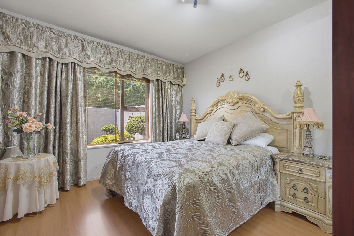 A well-maintained bedroom featuring laminate flooring and a large sliding window with decorative curtain pelmets.